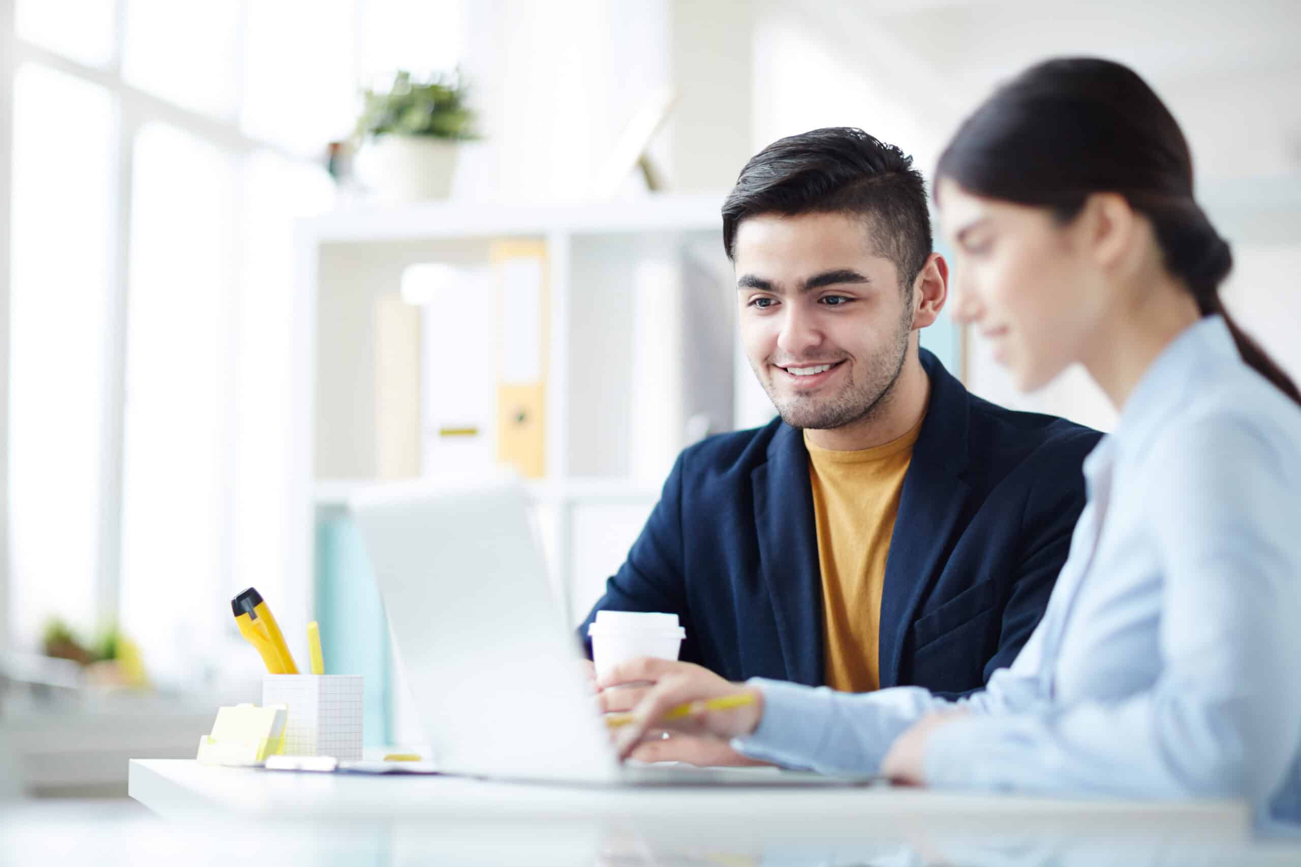 Two professionals working together at a desk with a laptop in an office setting.